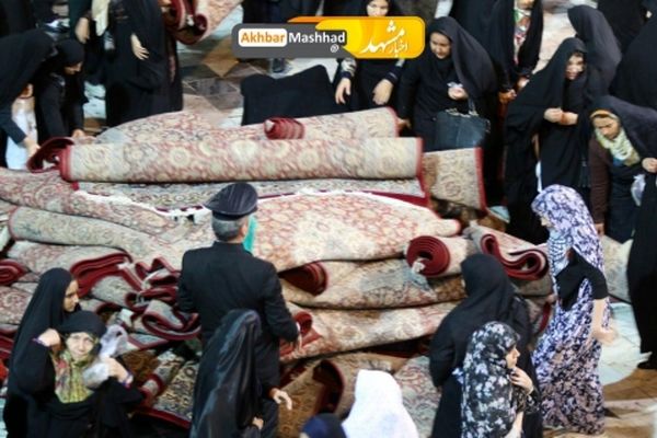 تلاش بانوان برای جمع آوری فرش های حرم رضوی در پی بارش شدید باران