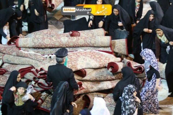 تلاش بانوان برای جمع آوری فرش های حرم رضوی در پی بارش شدید باران